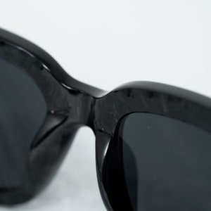 Puede incluir: Gafas de sol negras con una montura gruesa y texturizada y lentes oscuras.