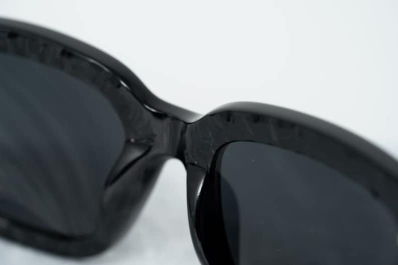 Puede incluir: Gafas de sol negras con una montura gruesa y texturizada y lentes oscuras.