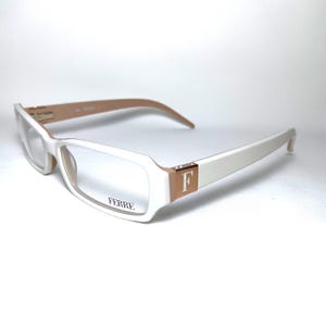Peut inclure: Lunettes rectangulaires blanches avec un accent brun et or sur le côté. Le nom de la marque "FERRE" est imprimé sur la monture.