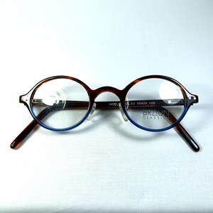 May include: Round eyeglasses with a brown tortoiseshell frame and blue accents. The lenses are clear, and the arms are dark brown. The brand name "BRAUN CLASSIC" is visible on the frame. The frame size is 53-45024-145.