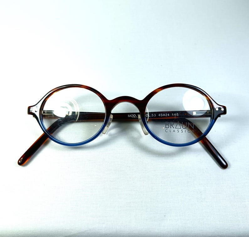 May include: Round eyeglasses with a brown tortoiseshell frame and blue accents. The lenses are clear, and the arms are dark brown. The brand name "BRAUN CLASSIC" is visible on the frame. The frame size is 53-45024-145.