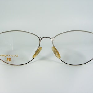 May include: Silver-toned eyeglasses with a clear lens and the text "Courr&egrave;ges" in gold lettering on the left frame.