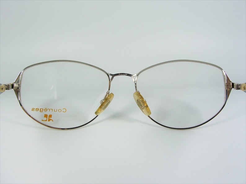 May include: Silver-toned eyeglasses with a clear lens and the text "Courr&egrave;ges" in gold lettering on the left frame.