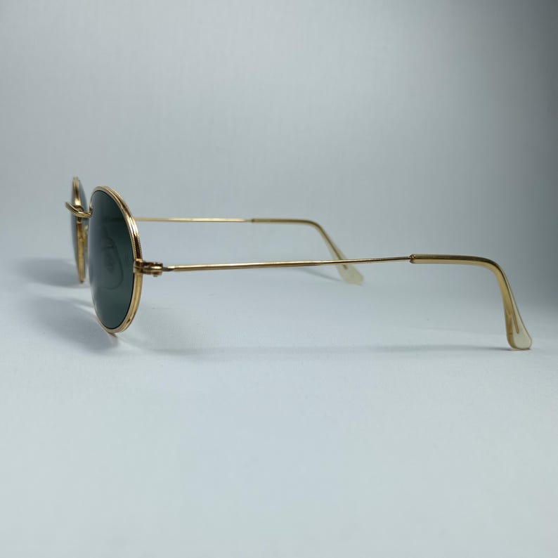 Puede incluir: Gafas de sol de metal dorado con lentes redondas verdes. Las gafas tienen un marco fino de metal y son de estilo cl&aacute;sico.