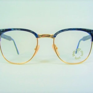 Op de afbeelding: Blauwe en gouden bril met een gouden metalen montuur en blauwe marmeren kunststof pootjes. De glazen zijn helder en de merknaam "Look" is op het rechter glas gedrukt.