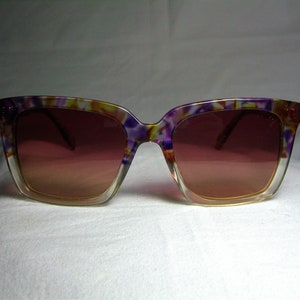 May include: Purple, yellow, and white patterned sunglasses with brown lenses.