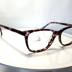 Peut inclure: Lunettes &agrave; motif &eacute;caille de tortue dans des tons de marron, noir et violet. Les montures sont de forme rectangulaire avec une l&eacute;g&egrave;re forme &oelig;il de chat. Les lunettes sont pr&eacute;sent&eacute;es sur une surface blanche.