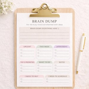 Op de afbeelding: Een houten clipboard met een gouden clip met een "Brain Dump" notitieblok. Het notitieblok heeft secties voor "Dringend", "Deze week" en "Later/Ideeën". Een witte pen met gouden accenten ligt aan de rechterkant. De tekst van het notitieblok bevat "Brain Dump Everything Here".