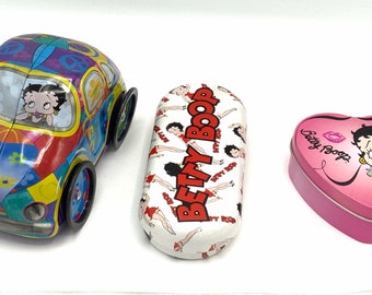 May include: Three tin containers featuring Betty Boop. One is a pink heart-shaped box, another is a white rectangular box with the text "Betty Boop" in red, and the third is a colorful toy car with Betty Boop driving.