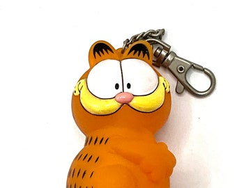Può includere: Portachiavi in ​​plastica arancione con il personaggio dei cartoni animati Garfield. Il portachiavi è in plastica e ha un anello di metallo.