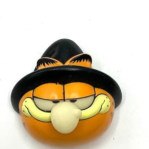 May include: Orange and black Halloween figurine of Garfield the cat wearing a witch's hat.