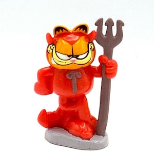 May include: A red devil Garfield figurine holding a grey pitchfork. The figurine is made of plastic and has a cartoonish style.