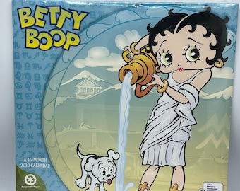 Puede incluir: Un calendario de 16 meses de 2010 con Betty Boop vestida como una diosa romana vertiendo agua de una jarra. El calendario tiene un fondo azul con símbolos del zodíaco y un perro blanco.