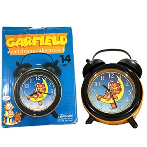 May include: Vintage Garfield "Sweet Dreams" alarm clock with a black frame and orange base. The clock face features Garfield on a crescent moon. The box reads "14 inches".