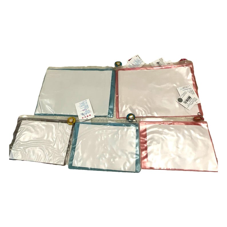 May include: A collection of clear, rectangular pouches with colored trim and zipper closures. The pouches have blue, pink, and white trim. Some pouches have tags attached. The pouches are likely for storage or organization.