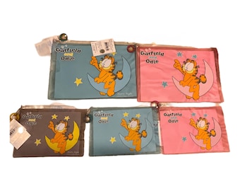 Può includere: Cinque astucci con cerniera a tema Garfield e Odie in vari colori: blu, rosa e marrone. Ogni astuccio presenta Garfield su una luna crescente con stelle. Il testo "Garfield and Odie" è stampato su ogni astuccio.