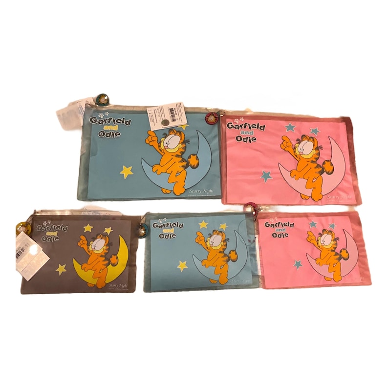 May include: Five Garfield and Odie themed zippered pouches in various colors: blue, pink, and brown. Each pouch features Garfield on a crescent moon with stars. The text "Garfield and Odie" is printed on each pouch.