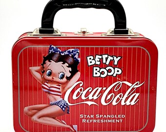 May include: Red metal lunchbox with a black handle. The lunchbox features a cartoon image of Betty Boop wearing a red, white, and blue swimsuit. The Coca-Cola logo is printed on the lunchbox with the text "Star Spangled Refreshment".