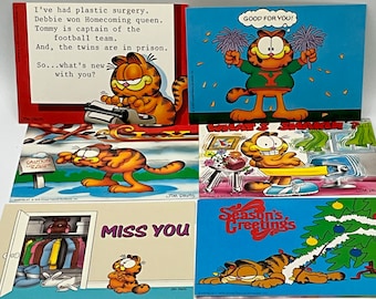 May include: A set of six Garfield comic postcards. The postcards feature different scenes with Garfield, including him typing on a typewriter, wearing a cheerleader uniform, and decorating a Christmas tree. The text on the postcards includes quotes from Garfield, such as "I've had plastic surgery" and "Good for you!"