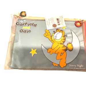May include: A Garfield and Odie pillowcase featuring Garfield sitting on a crescent moon with a yellow star. The pillowcase has the words "Starry Night" and "Garfield and Odie" printed on it. The pillowcase is in a clear plastic bag.