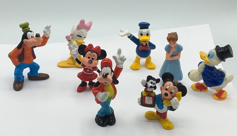May include: A collection of nine small plastic figurines of Disney characters, including Mickey Mouse, Minnie Mouse, Donald Duck, Goofy, and Daisy Duck. The figurines are brightly colored and feature various poses.