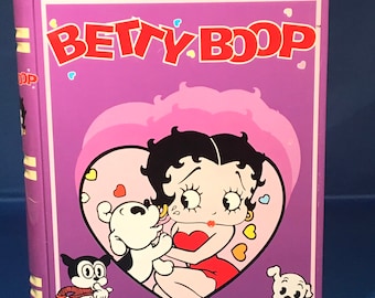 Peut inclure: Une boîte en métal en forme de livre de couleur violette avec une illustration de Betty Boop. La boîte représente Betty Boop dans une robe rouge avec un cadre en forme de cœur et deux chiens blancs. Le texte "BETTY BOOP" est imprimé en lettres rouges sur le devant de la boîte.