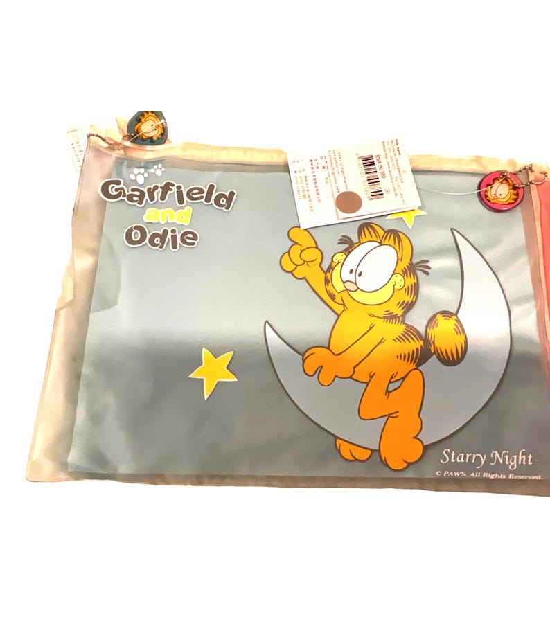 May include: A Garfield and Odie pillowcase featuring Garfield sitting on a crescent moon with a yellow star. The words "Starry Night" are printed on the pillowcase. The pillowcase is in a clear plastic bag.