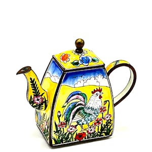 May include: A yellow teapot with a rooster design. The teapot is decorated with colorful flowers and has a blue and green rooster on the front. The teapot has a brass lid and spout.