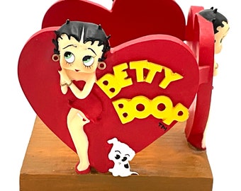 Könnte beinhalten: Roter herzförmiger Serviettenhalter mit einem Cartoon-Bild von Betty Boop, einem Hund und dem Text "BETTY BOOP" in gelben Buchstaben.