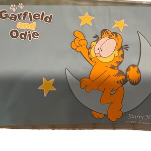 May include: A Garfield and Odie poster featuring Garfield sitting on a crescent moon, pointing upwards. The orange cat is surrounded by yellow stars against a blue background. The words "Garfield and Odie" are at the top.