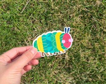 May include: A green and yellow caterpillar sticker with a red head and pink cheeks. The caterpillar has a friendly expression and is smiling.