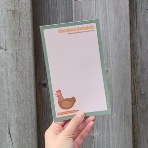 May include: A green and white notepad with the text "Chicken Scratch" and a brown chicken illustration. The notepad is designed by Mad Love Creative Co.