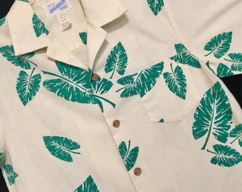 May include: A white button-down shirt with a green leaf pattern. The shirt has a collar and a pocket on the left side. The brand name "ANODADE" is visible on the collar.