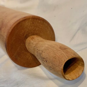 May include: A wooden rolling pin with a smooth, light brown finish. The rolling pin has a handle with a rounded, hollow end.