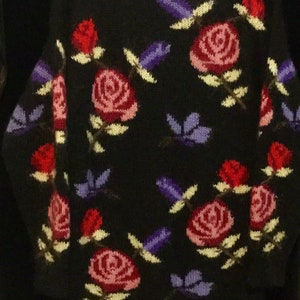 May include: Black knitted sweater with a floral pattern. The sweater features pink, red, and purple roses with green leaves and stems.