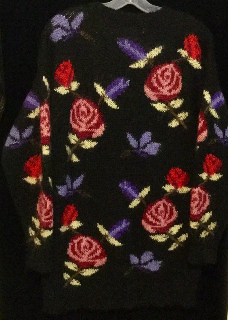 May include: Black knitted sweater with a floral pattern. The sweater features pink, red, and purple roses with green leaves and stems.