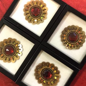 May include: Four framed gold and red embroidered flower embellishments with a red jewel center.