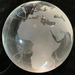 Op de afbeelding: Een matglazen globe met een gedetailleerde gegraveerde wereldkaart. De globe is helder en heeft een licht regenboogeffect door het licht dat van het oppervlak reflecteert.