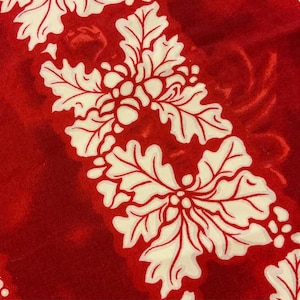 May include: Red fabric with a white floral pattern. The flowers are stylized and have a leaf-like design.