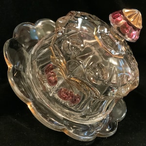 May include: A clear glass butter dish with a lid featuring a gold trim and pink glass cherries. The dish has a scalloped edge and is perfect for serving butter or other small snacks.