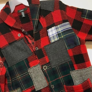 May include: A patchwork jacket featuring a red and black buffalo plaid pattern as the base. The jacket has multiple fabric patches in various patterns and colors, including gray, green, and blue. It has a button-up front and a collar. The brand tag "J.Crew" is visible.