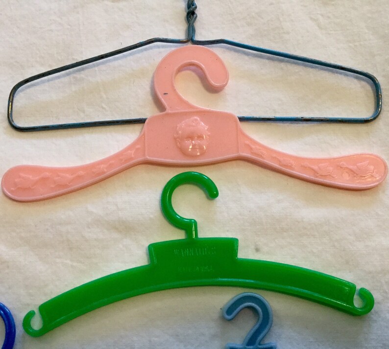 May include: Three plastic hangers, one pink with a child's face, one green with the word "remarkable" and one blue.