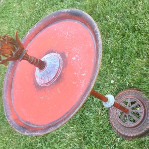 May include: A red metal bird bath with a decorative finial on top. The bird bath is on a stand with a round base.