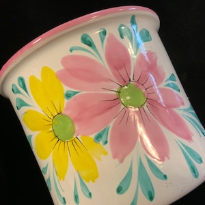 May include: White ceramic planter with a pink and yellow floral design. The planter has a wide rim and a rounded base.