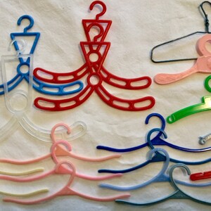 May include: A collection of ten plastic hangers in various colors, including clear, pink, red, blue, and green. Some hangers have a simple design, while others have a more intricate design with multiple loops.