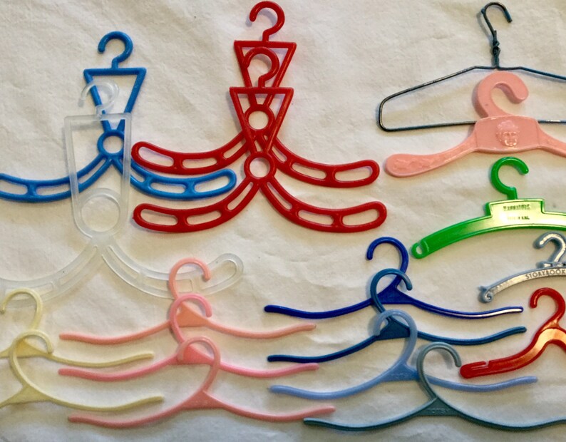 May include: A collection of ten plastic hangers in various colors, including clear, pink, red, blue, and green. Some hangers have a simple design, while others have a more intricate design with multiple loops.