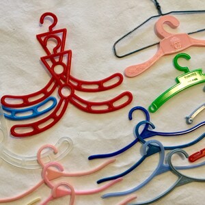 May include: A collection of plastic hangers in various colors, including red, blue, green, pink, and white. Some hangers are designed with multiple hooks, while others have a single hook. The hangers are made of a lightweight plastic material and are suitable for hanging clothes or other items.