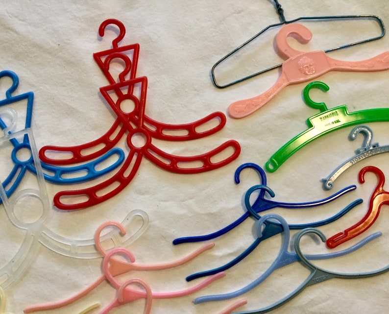 May include: A collection of plastic hangers in various colors, including red, blue, green, pink, and white. Some hangers are designed with multiple hooks, while others have a single hook. The hangers are made of a lightweight plastic material and are suitable for hanging clothes or other items.