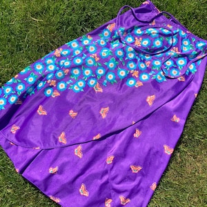 Op de afbeelding: Een paarse wikkelrok met een bloemenprint en vlindermotief. De rok heeft een strik sluiting aan de taille.