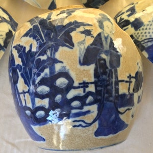 May include: A blue and white porcelain jar with a floral design and a figure in a robe. The jar is cracked and chipped, showing the beige clay underneath.